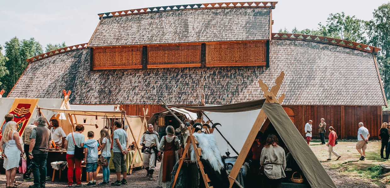 Teltleir foran en stor bygning (en viking Gildehall rekonstruksjon) med mennesker i historiske kostymer.