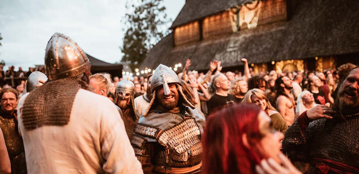 Folkemengde kledd som vikinger smiler med hendene i været utenfor et vikingbygg i Horten.